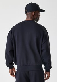 Černá mikina s volným střihem, žebrovanými manžetami a lemem. Měkká textura, minimalistický design, s kulatým výstřihem a spadlými rameny.