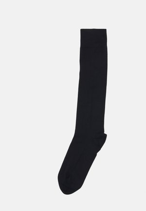 Zwarte knielange sok gemaakt van zacht materiaal, met een gladde textuur en een gestructureerde geribbelde boord aan de bovenkant voor een veilige pasvorm.