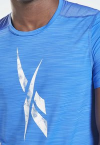 Blå atletisk t-shirt med subtila horisontella ränder, som har en stor vit grafisk logotyp på framsidan och texturerade axelinsatser.