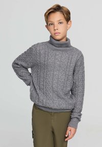 Szary sweter z golfem, wykonany na drutach, z fakturą w warkocze i ściągaczami przy mankietach, w połączeniu z oliwkowymi spodniami. Prosty, casualowy design.