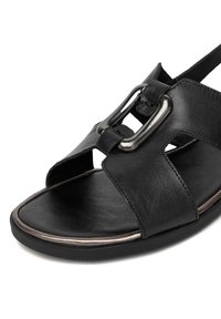 Černá kožená sandála se širokým páskem, kovovými přezkami, otevřenou špičkou a texturovanou podrážkou pro lepší přilnavost.