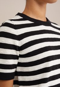 Svart och vit randig stickad tröja med ribbad rund halsringning, med texturerade mönster i växlande ränder och korta ärmar.