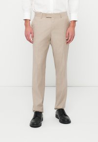 Bézs színű, textúrált szövetből készült, testre szabott nadrág, közepes derékkal és egyenes szárral, fekete bőrcipővel párosítva.