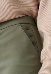 Olivově zelená sukně s plochým pasem a třemi ladícími knoflíky na boku. V kombinaci se světle růžovým žebrovaným svetrem.
