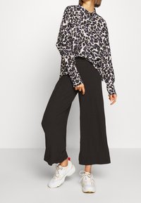 Blouse à imprimé léopard à manches longues avec col à boutons ; associée à un pantalon large en côte noir et des baskets de sport blanches.