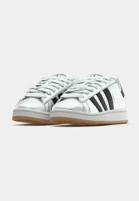 Sidabriniai sintetinių medžiagų sportbačiai su juodomis juostelėmis, suvarstyti raišteliais, apvaliais noseliais ir guminiais padais; prekės ženklas ant liežuvėlio ir kulno.