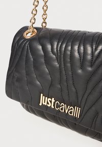 Black quilted leather handbag with gold chain strap and gold "Just Cavalli" logo on front flap closure.