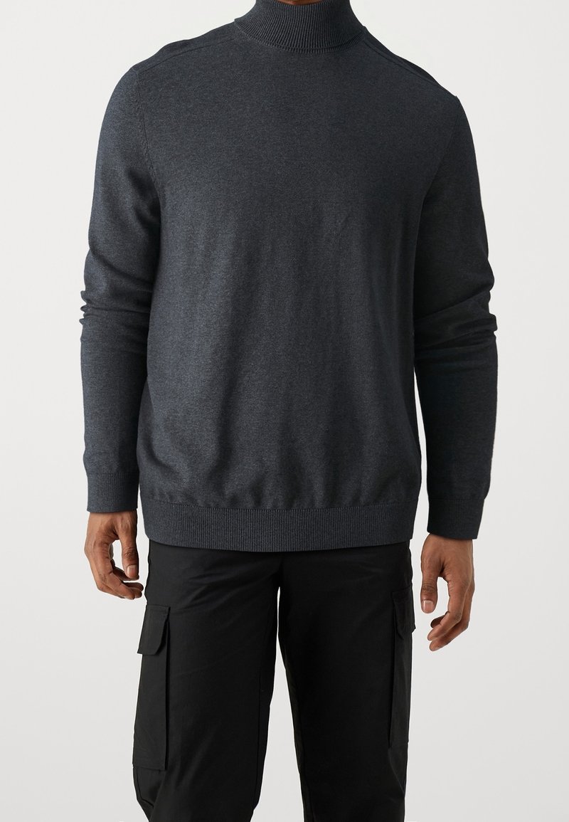 Grå turtleneck-tröja i mjukt material, med långa ärmar och ribbade mudd. Designen är åtsittande med en slät yta.