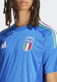 Maillot de sport bleu à manches courtes, arborant le logo de l'équipe nationale italienne et quatre étoiles. Accentué de rayures rouges, vertes et blanches.