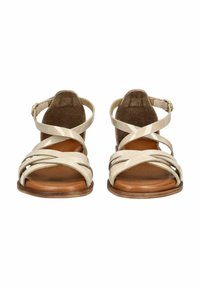 Beige Riemchensandalen mit einem eleganten Lackfinish. Sie haben mehrere überkreuzte Riemen und eine braune flache Sohle, ergänzt durch einen verstellbaren Knöchelriemen.