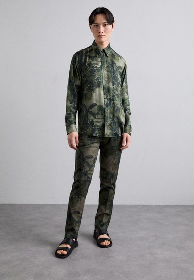 Green patterned shirt and pants made of lightweight fabric, featuring floral and leaf designs. Paired with black sandals on bare feet.