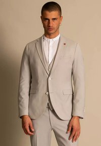 Lichtgrijs pak gemaakt van een gladde stof, met een getailleerd ontwerp, notch revers en een kleine rood accent op het revers. Witte overhemd eronder.