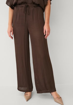 Bruine, lichtgewicht, wijdvallende broek met een elastische tailleband en een trekkoorddetail, gecombineerd met beige puntige flats. Gladde textuur.