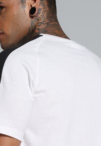 Camiseta de manga corta en blanco con detalles en negro en los hombros. Material de algodón con una textura suave. Presenta un cuello redondo clásico y un ajuste relajado.