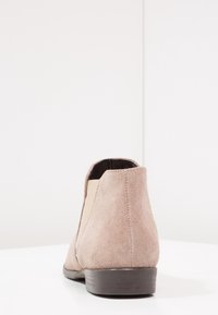 Beige mokka nilkkuri, jossa on joustavat sivupaneelit, pyöreä kärki, matala korko ja rakenteellinen pinta; yksinkertainen ja siisti muotoilu.