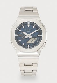 Montre Casio G-Shock en acier inoxydable argenté avec un cadran bleu foncé, des index lumineux, un affichage numérique et un design robuste. Résistante à l'eau jusqu'à 20 bars.