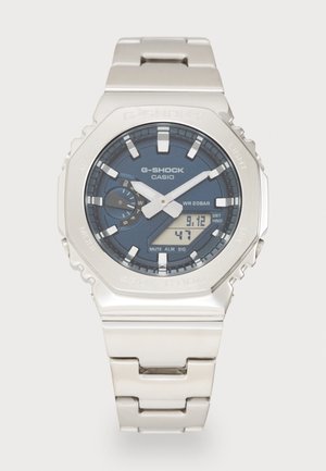 Reloj Casio G-Shock de acero inoxidable plateado con un dial azul oscuro, marcadores luminosos, pantalla digital y un diseño resistente. Resistente al agua hasta 20 bar.