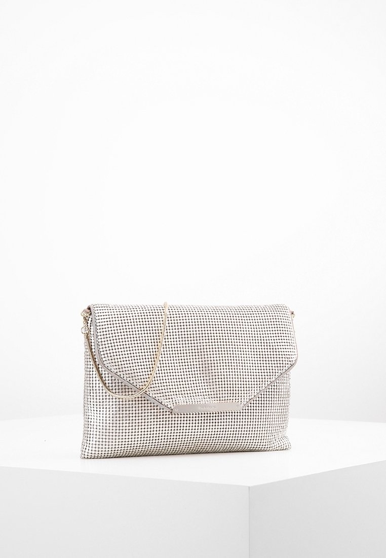 Pochette en maille argentée avec une fine chaîne dorée reposant sur un socle blanc sur un fond blanc uni.