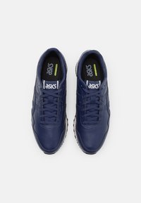 Zapatillas de cuero azul marino con un acabado texturizado, que presentan un logo de ASICS blanco y cordones, diseño de bajo perfil y suelas de goma.