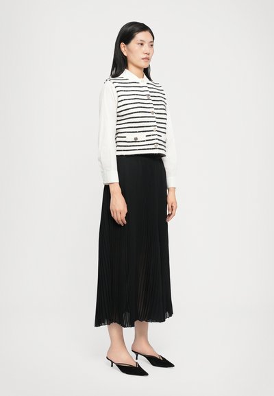 Randig svart och vit kort topp med knapplås framtill, lager på lager över en lång svart plisserad kjol. Svarta slingbackklackar kompletterar outfiten.