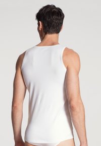 White cotton tank top, close-fitting design, sleeveless with a smooth texture. Features a rounded neckline and straight hem at the waist.