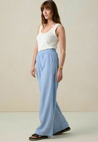 Lichtblauwe, wijde broek met een textuurstof en een elastische tailleband. Gecombineerd met een witte mouwloze top en zwarte sandalen.