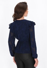 Marineblå bluse med gennemsigtige lange ærmer, volanger, blomstret tekstur og en tætsiddende talje med en peplum-silhuet.