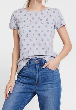 Jasnoszara koszula z krótkim rękawem z drobnym wzorem wielokolorowych buteleczek perfum, lekko włożona do wysokich, niebieskich dżinsów.