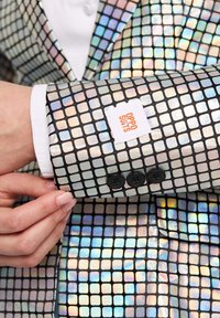 Svetleči črn suknjič z iridescentnim kvadratnim vzorcem, z belo etiketo "OPPO SUITS" in tremi črnimi gumbi na manšeti.