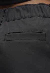 Primo piano di pantaloni neri con elastico in vita e una tasca posteriore orizzontale con cuciture visibili.