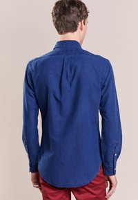 Laivan sininen pitkähihainen paita, jossa on nappikaulus, pyöristetty helma ja yksinappiset hihansuut, valmistettu tekstuurisesta kankaasta.