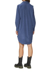 Hellblauses Cordhüftkleid mit langen Ärmeln, geknöpften Manschetten und asymmetrischem Saum. Getragen mit schwarzen Stiefeletten mit dicker Sohle.