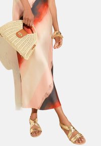 Verzierte goldene Sandalen, ein gemustertes Kleid in Pink und Rot sowie eine gewebte beige Handtasche mit einem Lederakzent. Sanfte Texturen und fließende Formen.