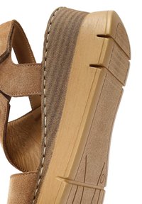 Brown suede wedge sandal showing textured upper, beige sole with grooves, and contrasting stitching along the edge.
