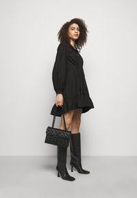 Czarna sukienka z guzikiem, z bufkami i falbaniastym dołem. Połączona z czarnymi, sięgającymi do kolan, spiczastymi botkami oraz fakturowaną czarną torebką.