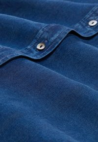 Blauer Denim-Stoff mit glatter Textur und subtilen Variationen. Verfügt über silberne Knopfdetails und Nähte, die ein klassisches Design unterstreichen.