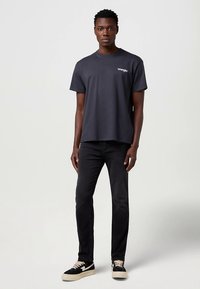 Tamsiai pilka trumpomis rankovėmis marškinėliai su apvalia apykakle; ant krūtinės mažas baltas logotipas. Derinami su juodais džinsais ir juodais sportbačiais.