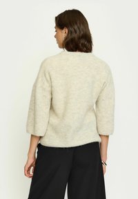 Heller beiger, übergroßer Pullover mit weicher Textur, Dreiviertelärmeln und rundem Halsausschnitt, kombiniert mit lockeren schwarzen Hosen.