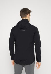 Veste noire imperméable avec capuche, dotée d'un logo dans le dos, de manches longues et d'un accent réfléchissant près de l'ourlet.