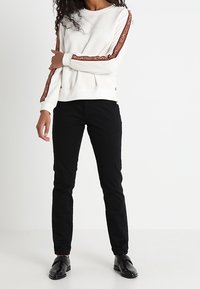 Felpa bianca con strisce laterali rosse e dettaglio del logo. Abbinata a pantaloni aderenti neri e scarpe nere con texture. Un semplice outfit casual.