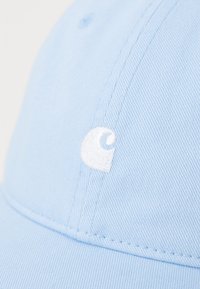 Cappellino azzurro chiaro realizzato in tessuto testurizzato con logo bianco ricamato. Il design include una visiera curva e dettagli cuciti.