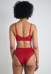 Crveno bikinis set u kojem se ističe elegantan dizajn, podesive naramenice i gaćice visokog struka. Glatka, rastezljiva tkanina bez vidljivih uzoraka.
