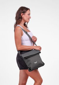 Černá látková taška přes rameno s překlopeným vrškem, stříbrnými doplňky a decentním logem. Nastavitelný popruh pro všestranné možnosti nošení.