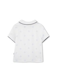 Polo blanc avec motif de logo bleu clair, manches courtes et bordure de col marine. Le tissu semble lisse et légèrement texturé.