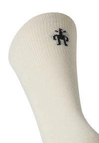 Weiße Socke mit geripptem Textur, die ein kleines schwarzes Logo am Bündchen trägt. Das Design ist einfach und funktional.
