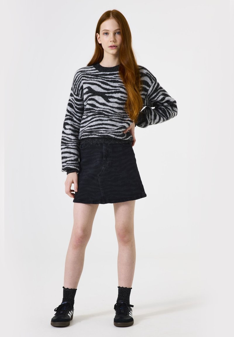 Zwart-wit gestreepte sweater van zachte stof, gecombineerd met een zwarte denim rok. Zwarte sneakers en gemusterde sokken maken de outfit compleet.