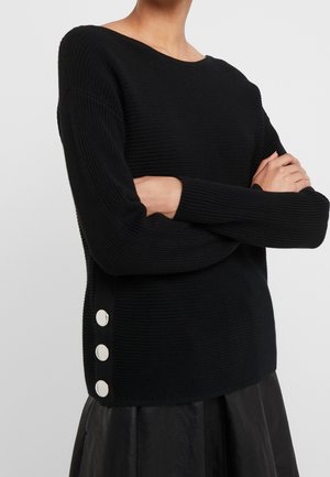 Schwarzer gestrickter Pullover mit geripptem Muster, weiter Ausschnitt und drei dekorativen silbernen Knöpfen auf der linken Seite.