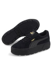 Sneakers in suede nero con suola spessa, suola in gomma testurizzata e logo Puma dorato. Presentano un accento in pelle nera liscia sul lato.