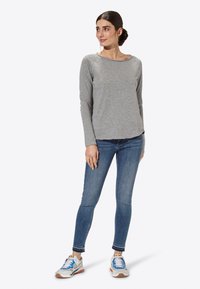 Maglione grigio a maniche lunghe con scollo ampio, abbinato a jeans skinny blu e sneakers bianche con dettagli colorati.