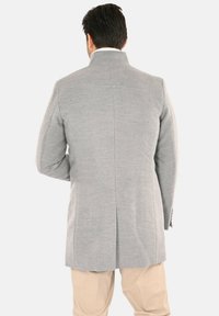 Cappotto in misto lana grigio con taglio sartoriale, collo alto e un'unica spacco sul retro. Presenta una texture sottile e linee pulite.